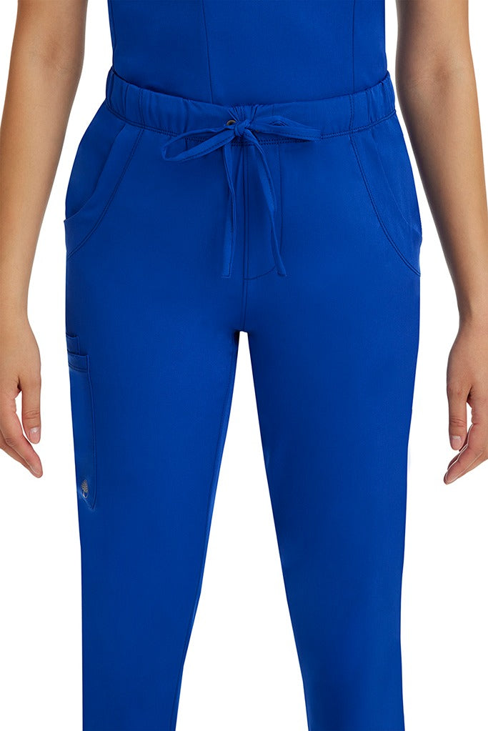 A female LPN wearing a pair of HH-Works Women's Rebecca Multi-Pocket Drawstring Pants in Galaxy Blue featuring 2 front slip pockets with a cargo pocket at the wearer's right leg.