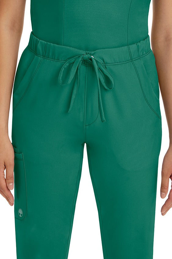 A female LPN wearing a pair of HH-Works Women's Rebecca Multi-Pocket Drawstring Pants in Hunter Green featuring 2 front slip pockets with a cargo pocket at the wearer's right leg.
