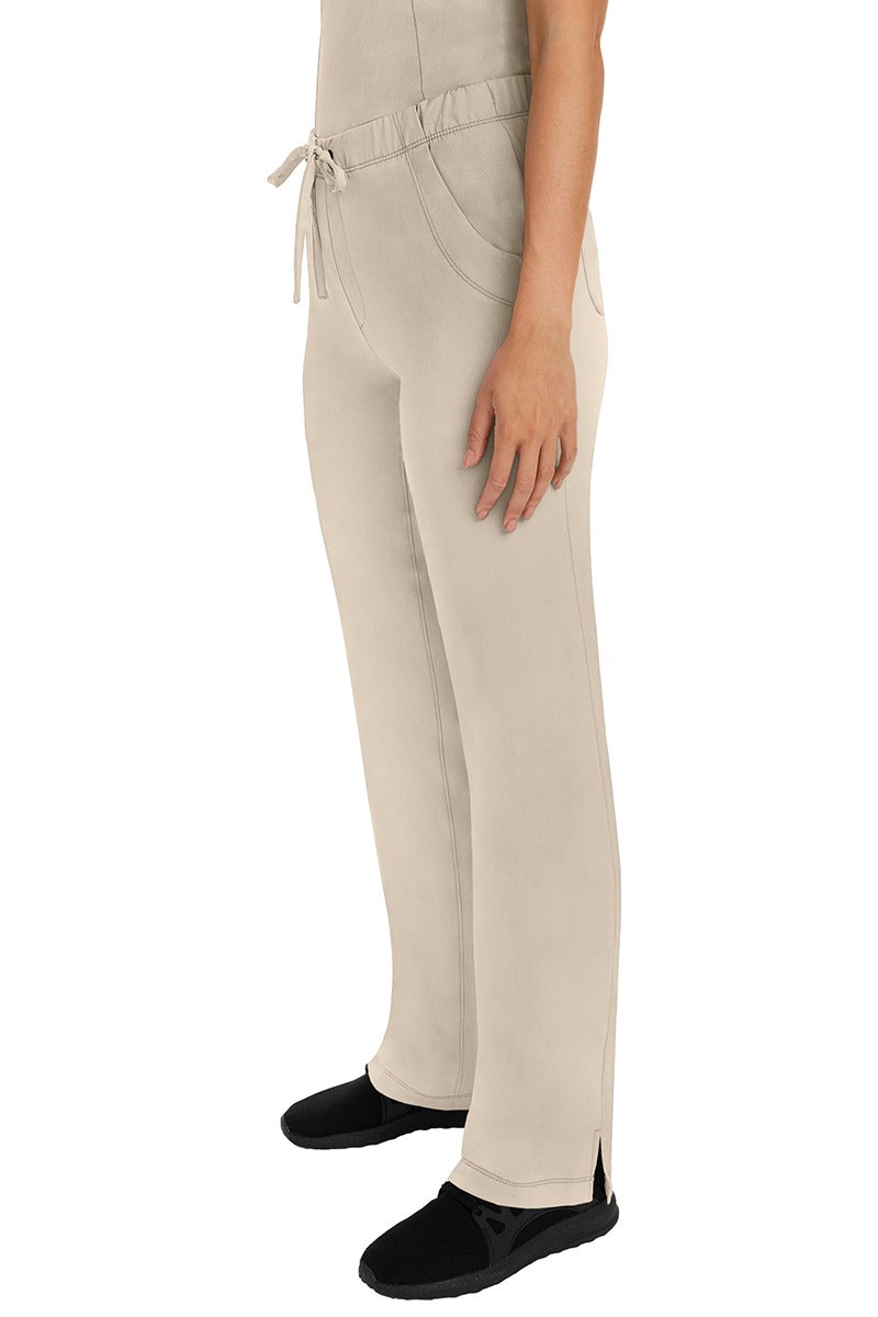 A woman Home Care Registered Nurse wearing a pair of HH-Works Women's Rebecca Multi-Pocket Drawstring Pants in Khaki featuring side slits for additional range of motion.