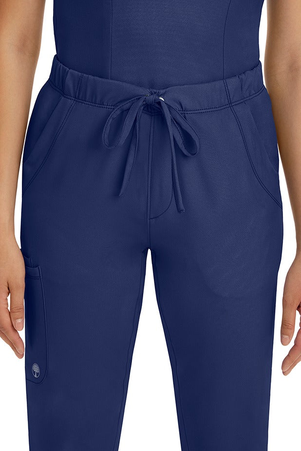 A female LPN wearing a pair of HH-Works Women's Rebecca Multi-Pocket Drawstring Pants in Navy featuring 2 front slip pockets with a cargo pocket at the wearer's right leg.