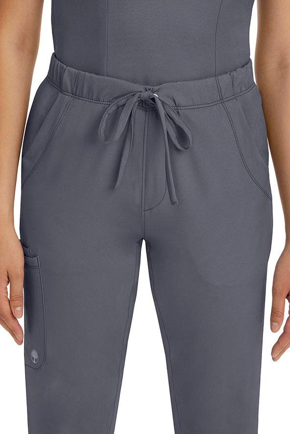 A female LPN wearing a pair of HH-Works Women's Rebecca Multi-Pocket Drawstring Pants in Pewter featuring 2 front slip pockets with a cargo pocket at the wearer's right leg.