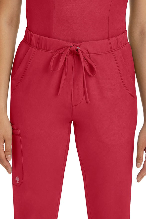 A female LPN wearing a pair of HH-Works Women's Rebecca Multi-Pocket Drawstring Pants in Red featuring 2 front slip pockets with a cargo pocket at the wearer's right leg.