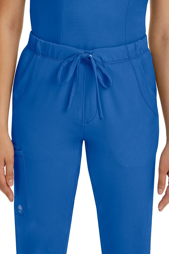 A female LPN wearing a pair of HH-Works Women's Rebecca Multi-Pocket Drawstring Pants in Royal featuring 2 front slip pockets with a cargo pocket at the wearer's right leg.