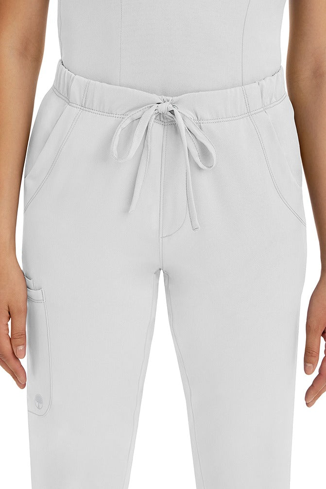 A female LPN wearing a pair of HH-Works Women's Rebecca Multi-Pocket Drawstring Pants in White featuring 2 front slip pockets with a cargo pocket at the wearer's right leg.
