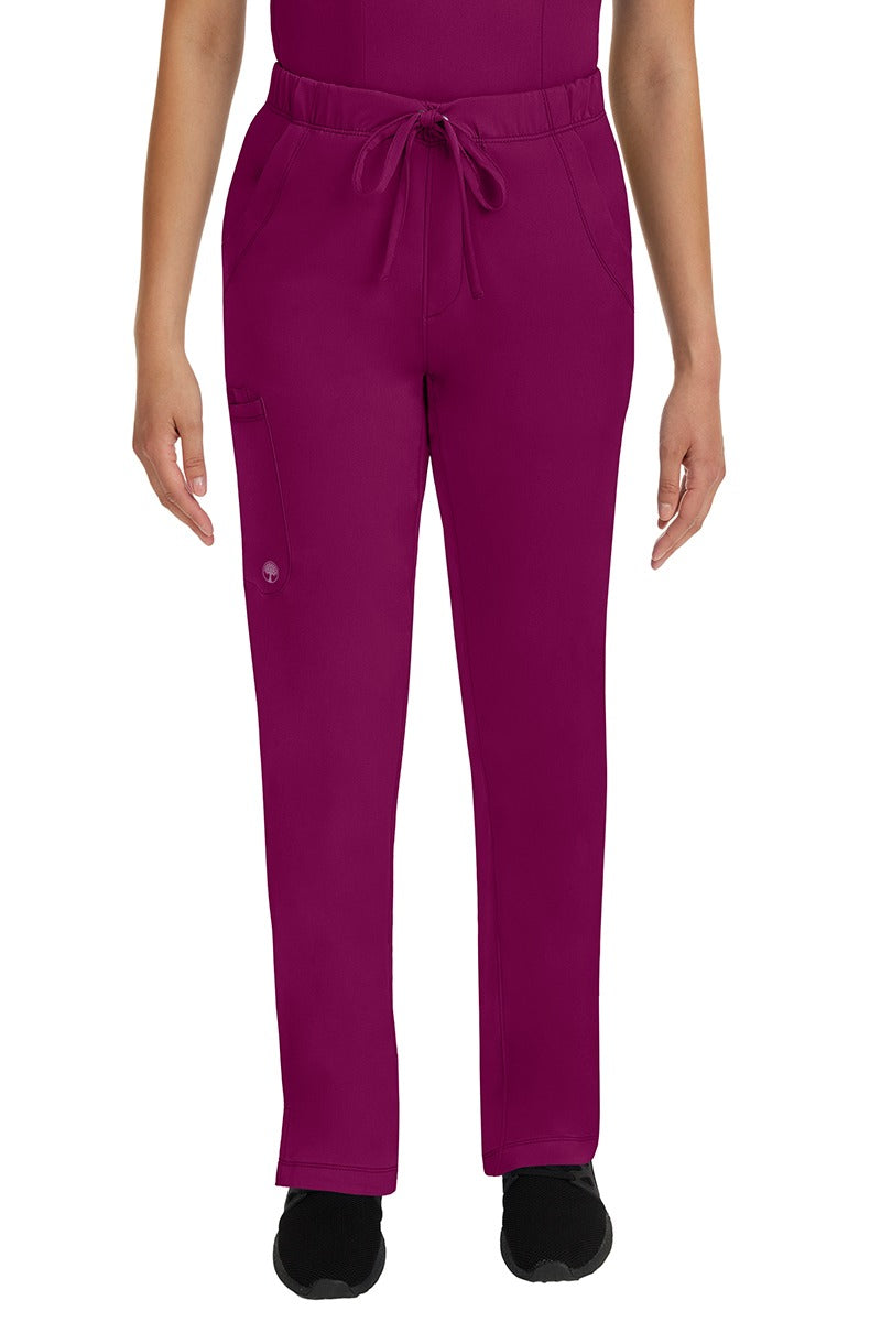 A young lady LPN wearing an HH Works Women's Rebecca Multi-Pocket Drawstring Pant in Wine featuring n all elastic waistband with a drawstring tie front.