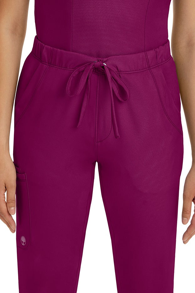 A female LPN wearing a pair of HH-Works Women's Rebecca Multi-Pocket Drawstring Pants in Wine featuring 2 front slip pockets with a cargo pocket at the wearer's right leg.
