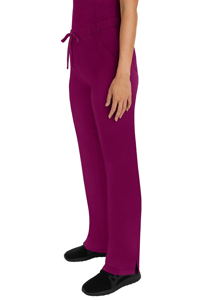 A woman Home Care Registered Nurse wearing a pair of HH-Works Women's Rebecca Multi-Pocket Drawstring Pants in Wine featuring side slits for additional range of motion.
