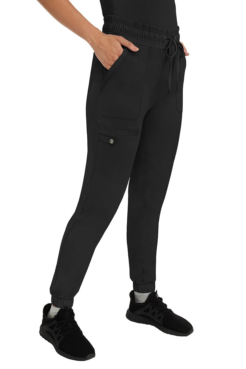 A female LPN wearing an HH Works Women's Renee Jogger Scrub Pant in Black featuring 2 front patch pockets & 1 cargo pocket the wearer's right side leg.