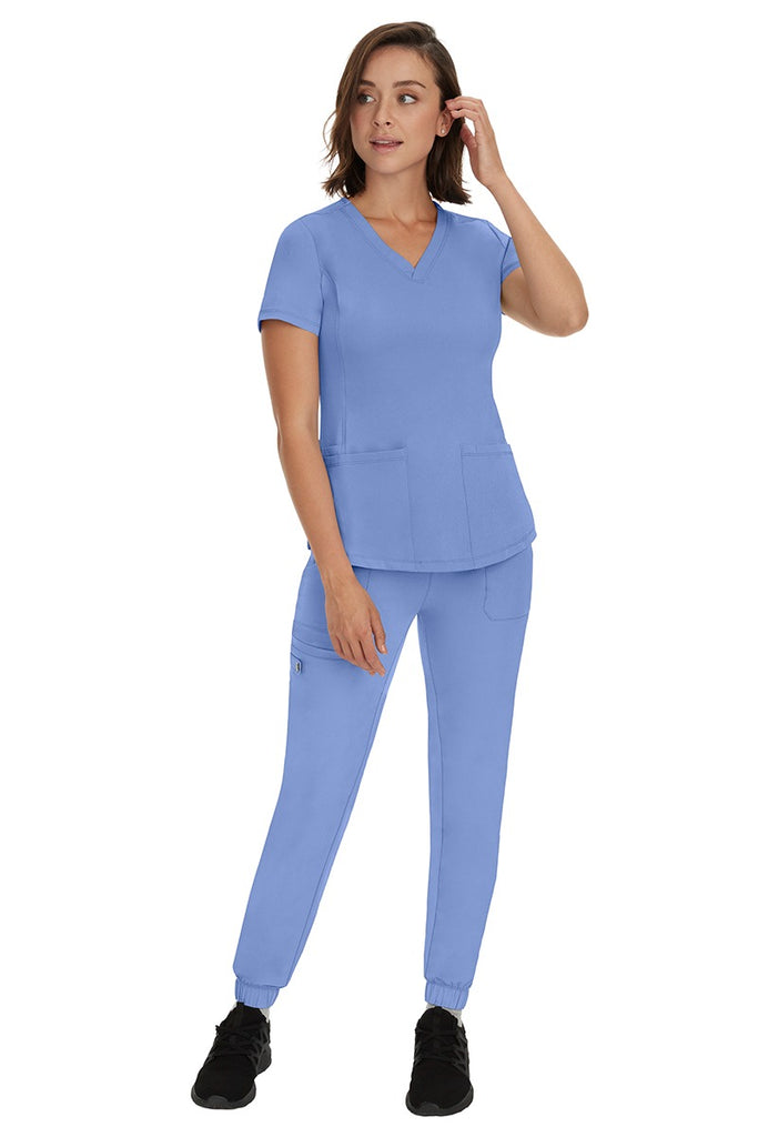 A young female RN wearing an HH Works Women's Renee Jogger Scrub Pant in Ceil featuring a modern fit with an elastic waist.