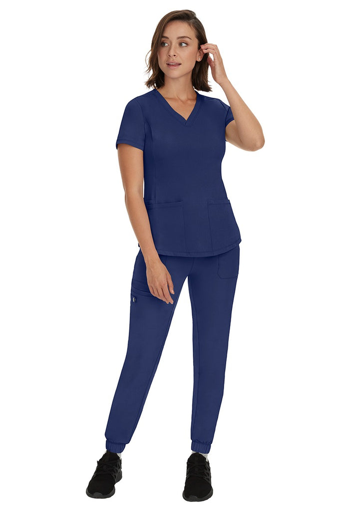 A young female RN wearing an HH Works Women's Renee Jogger Scrub Pant in Navy featuring a modern fit with an elastic waist.