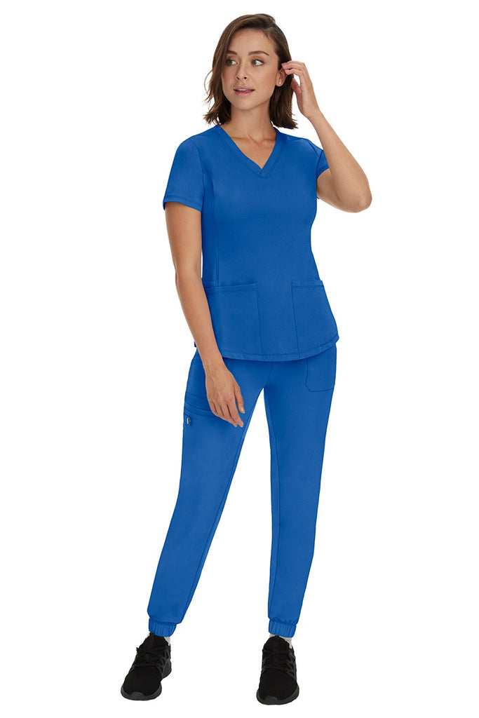 A young female RN wearing an HH Works Women's Renee Jogger Scrub Pant in Royal featuring a modern fit with an elastic waist.