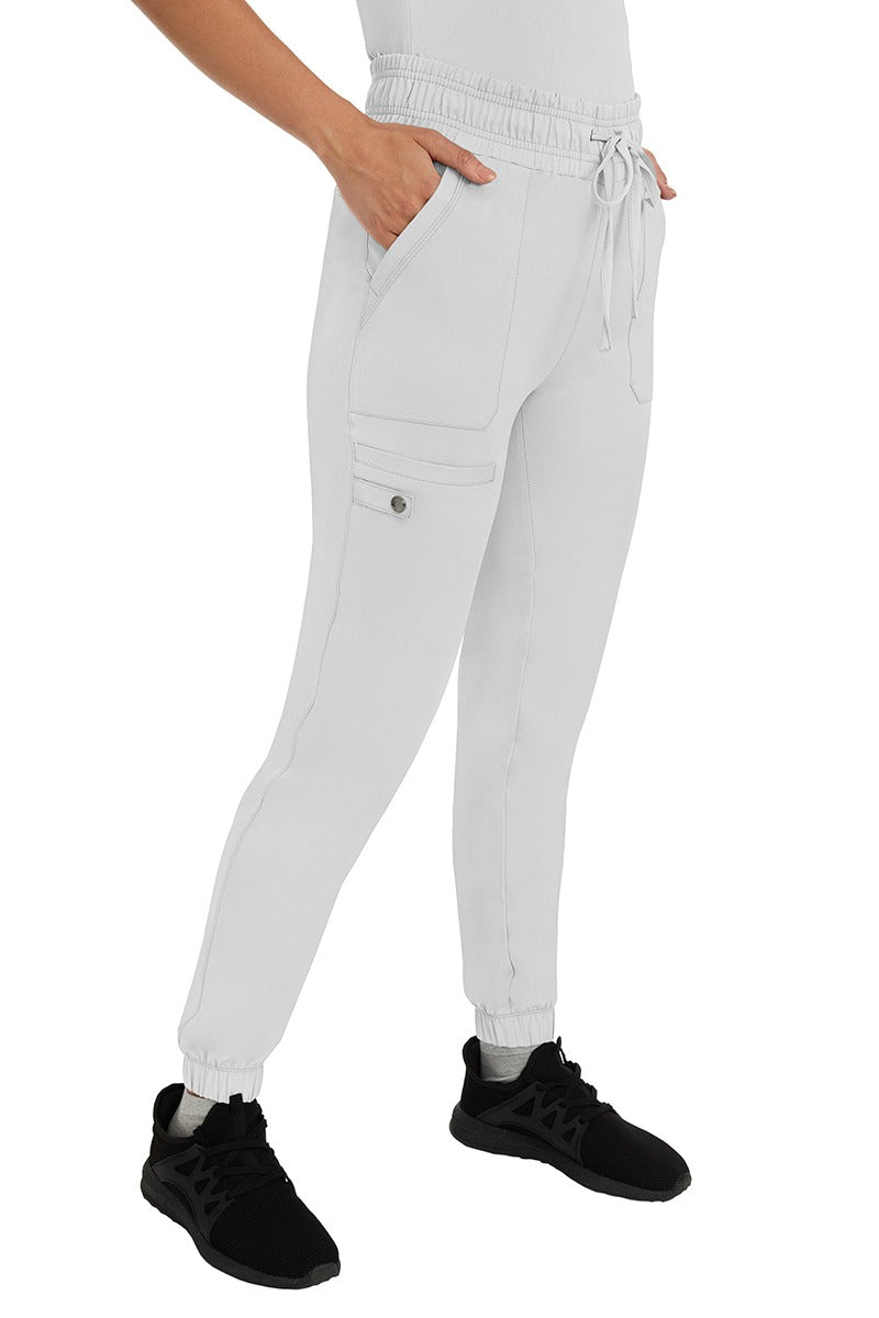 A female LPN wearing an HH Works Women's Renee Jogger Scrub Pant in White featuring 2 front patch pockets & 1 cargo pocket the wearer's right side leg.