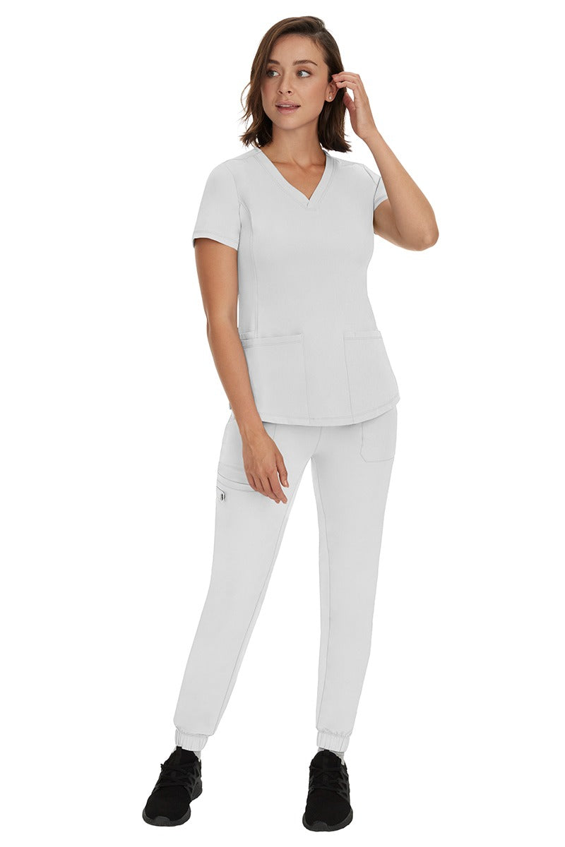 A young female RN wearing an HH Works Women's Renee Jogger Scrub Pant in White featuring a modern fit with an elastic waist.