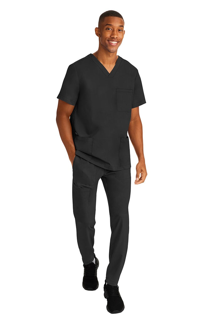A young male RN wearing an HH-Works Men's Ryan Multi-Pocket Cargo Scrub Pant in Black featuring an easy care fabric that is quick drying, moisture wicking, and ultra-flexible.