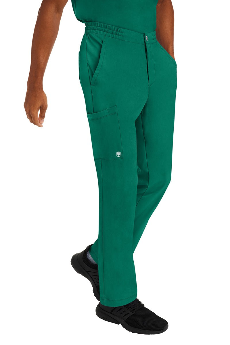 A young male CNA wearing a pair of HH-Works Men's Ryan Multi-Pocket Cargo Scrub Pants in Hunter Green featuring two front patch pockets.