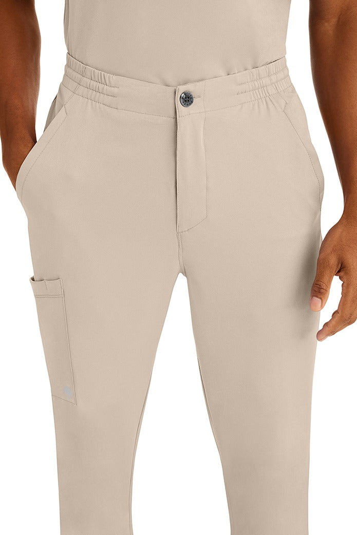 A young man wearing a Men's Ryan Multi-Pocket Cargo Scrub Pant from HH Works in Khaki featuring a super comfortable stretch fabric made of 91% polyester & 9% spandex.