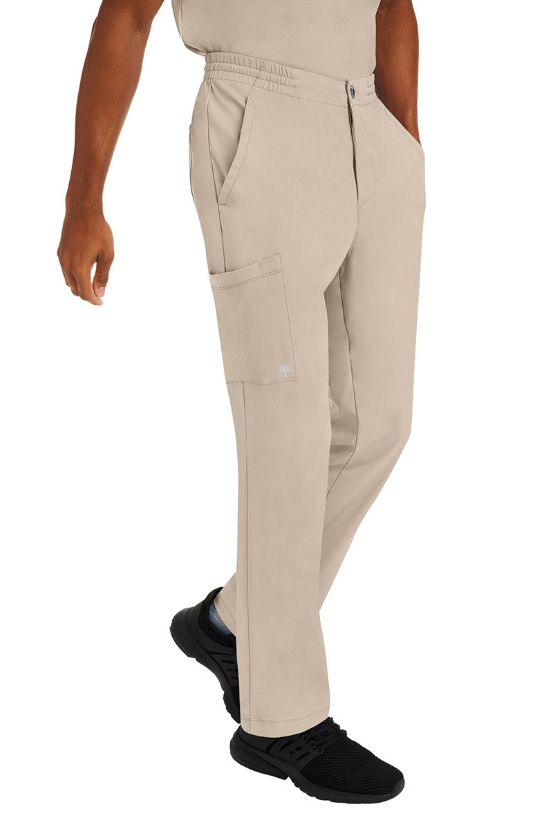A young male CNA wearing a pair of HH-Works Men's Ryan Multi-Pocket Cargo Scrub Pants in Khaki featuring two front patch pockets.