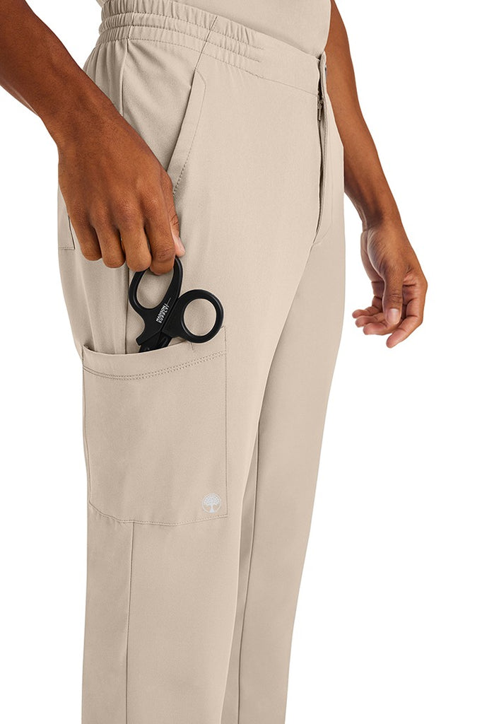 A male nurse wearing an HH-Works Men's Ryan Multi-Pocket Cargo Scrub Pant in Khaki featuring a total of 6 pockets for all of your on the job storage needs.