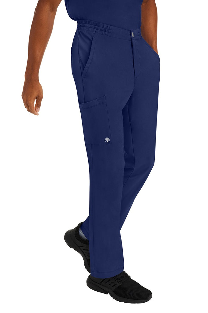 A young male CNA wearing a pair of HH-Works Men's Ryan Multi-Pocket Cargo Scrub Pants in Navy featuring two front patch pockets.
