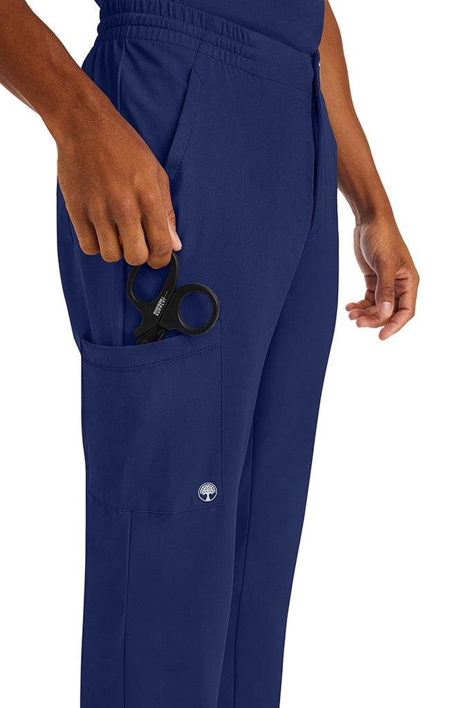 A male nurse wearing an HH-Works Men's Ryan Multi-Pocket Cargo Scrub Pant in Navy featuring a total of 6 pockets for all of your on the job storage needs.