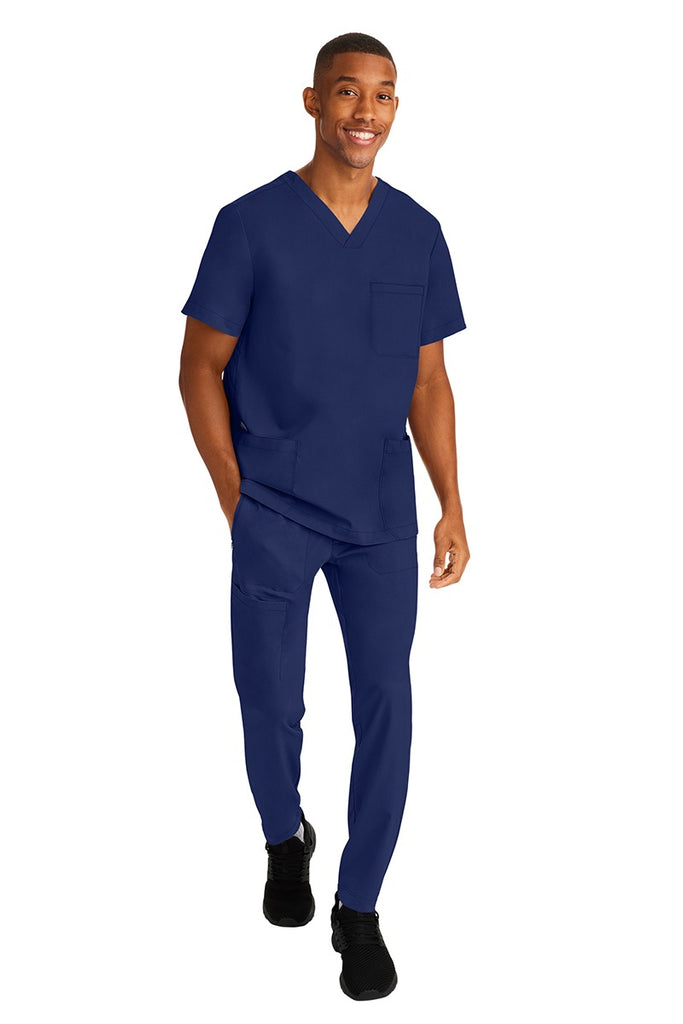 A young male RN wearing an HH-Works Men's Ryan Multi-Pocket Cargo Scrub Pant in Navy  featuring an easy care fabric that is quick drying, moisture wicking, and ultra-flexible.