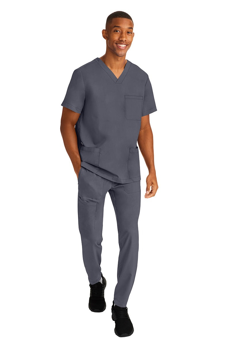 A young male RN wearing an HH-Works Men's Ryan Multi-Pocket Cargo Scrub Pant in Pewter  featuring an easy care fabric that is quick drying, moisture wicking, and ultra-flexible.