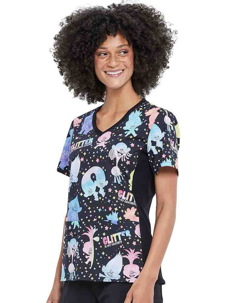 A young female Psychiatric Nurse wearing a Tooniforms Women's V-neck Knit Panel Printed Scrub Top in "Glitter Trolls" featuring two front patch pockets.