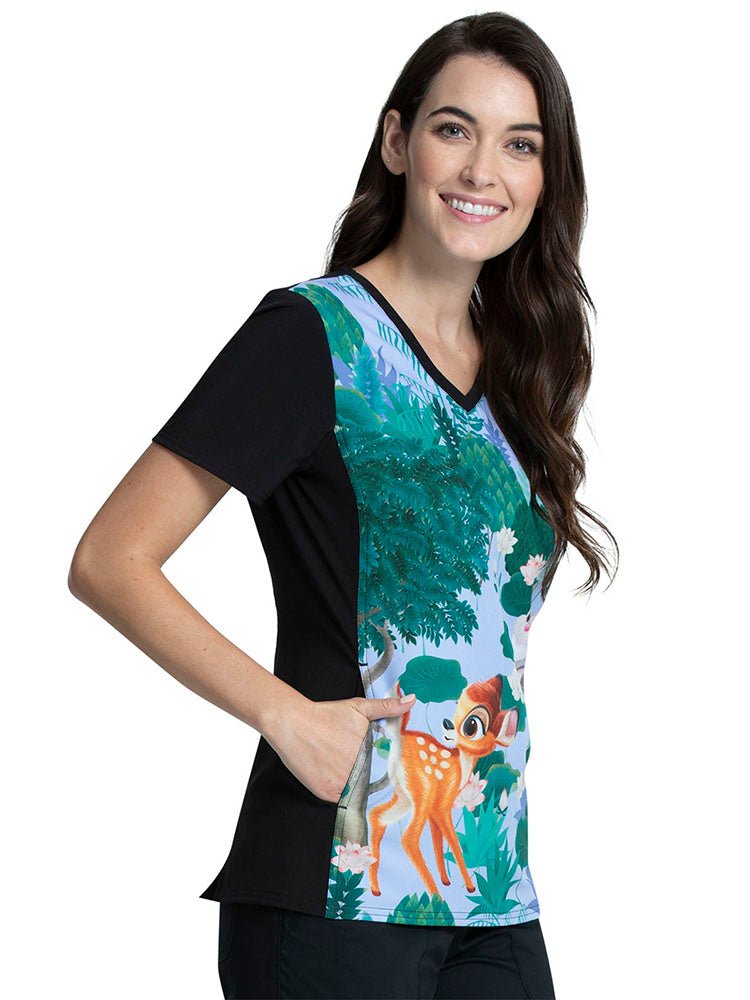 A young female nurse wearing a Tooniforms Women's V-neck Printed Scrub Top in "Forest Frolic" featuring solid knit panels at the sides.
