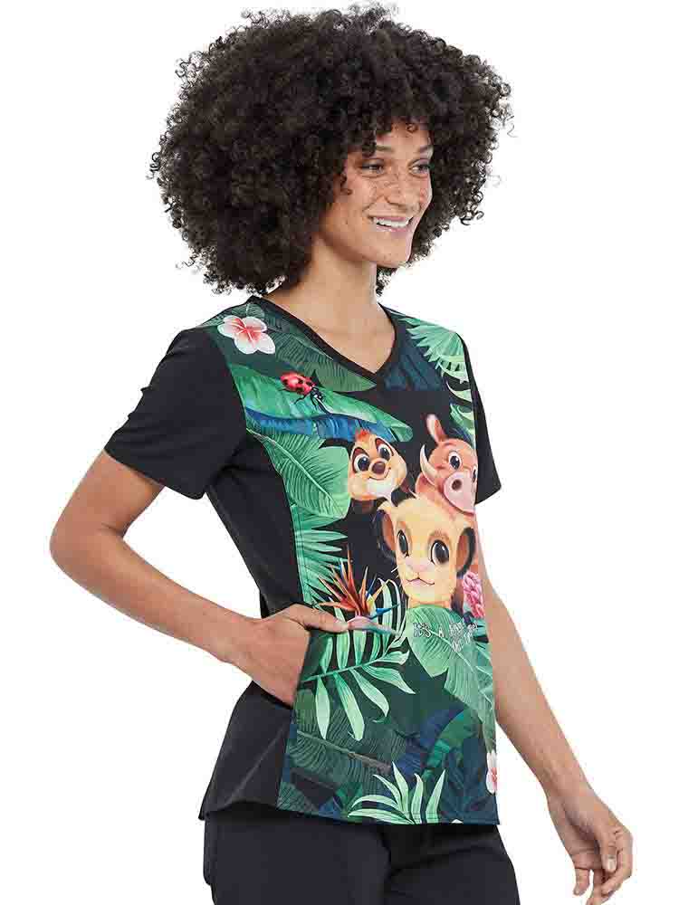 A young female Nurse wearing a Tooniforms Women's V-neck Print Scrub Top in "Wild Things" featuring solid knit panels at the sides and back.