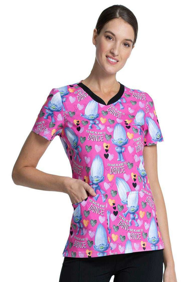 A young female Pediatric Nurse wearing a Tooniforms Women's V-Neck Print Top in "Diamond Dance" featuring DreamWorks Trolls throughout the design. 