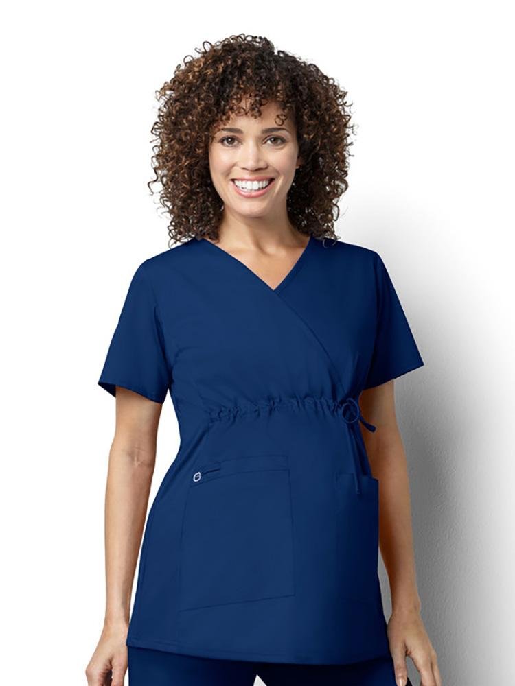 A pregnant Nurse Anesthetist wearing a Women's Maternity Mock Wrap Scrub Top from WonderWink in navy size extra small featuring an adjustable drawstring at front empire waist and added utility loop.